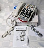 Phone assembled on box with handset, cords, wall-mount bracket, manual and line cord visible