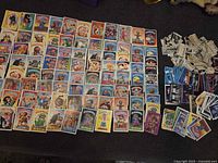 Overview of full lot: Garbage Pail Kids cards arranged in rows, Monster Laffs bills, assorted blue and black trading cards