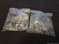 Two clear bags filled with metal Oakland Raiders pins on dark surface