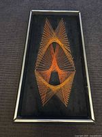 Full view of framed orange string art on black background