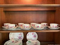 cabinet shelf with eight teacups on saucers showing floral pattern