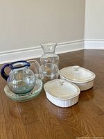Group shot of all kitchenware items including ceramic casseroles, glass carafe, coffee pot, stemless glasses, and plates