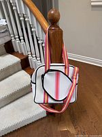 Front view of white perforated tote with striped strap draped over stair post