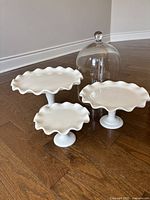 three white pedestal stands and glass cloche on wood floor