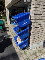 Full view of dolly holding three blue bins (bins not included) leaning against wall