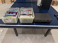 Overall lot showing two bins of VHS tapes and Samsung VCR on table