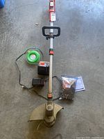 Full view of string trimmer with batteries, charger, trimmer line coil and sealed spool