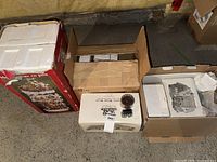 Three boxed items including red Gingerbread Tree House carton, white Department 56 styrofoam boxes in open cartons
