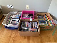 Four containers filled with DVDs and VHS tapes on floor