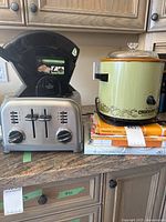 Overall lot showing toaster with bagel slicer on top, slow cooker, stack of cookbooks
