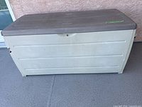 Front view of beige resin deck box with brown lid