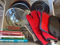 Drawer with frying pans, lids, oven mitts, baking pans, cookbooks