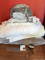 Stack of bedding items with alarm clock and boxed accessory on floor