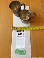 Two sterling silver cups beside measuring tape