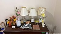 Overview of lamps, art glass bowl, wax warmer, clock, flowers, doll on dresser top