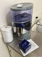 Full view of dispenser with replacement filter cartridge, sealed blue filter box and manual on countertop