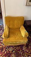 Front view of gold velour lounge chair showing tufted back, seat cushion, bolster pillows and carved wood frame
