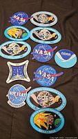 All 11 embroidered NASA and NOAA patches laid out on dark fabric