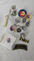 Group shot of eleven military pins, ribbon bar and Ranger patch on white background