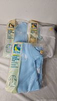 Three packaged infant sleeping bags, two blue one white