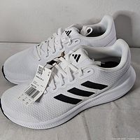 Side view of both sneakers showing white mesh upper and black stripes with tag attached