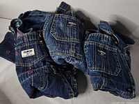 Three denim overalls overlapped; visible OshKosh labels