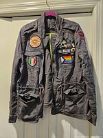 Full front view of grey Express jacket showing overall style, drawstring waist, zipper, pockets and attached patches and pins.