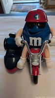 Front view of blue M&M character riding red motorcycle candy dispenser
