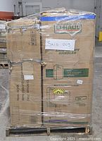 Front view of pallet wrapped in plastic showing U-Haul moving box and tall sofa parts cartons