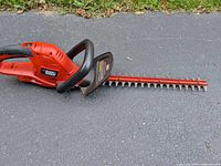 Full view of Black & Decker orange electric hedge trimmer lying on asphalt