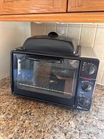 Front view of black Elite Cuisine toaster oven showing glass door, control knobs and grill-griddle lid