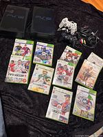 Two PS2 consoles, controllers, cables, and Xbox 360 games laid out
