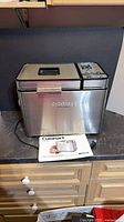 Full view of Cuisinart stainless steel bread maker with manual in front