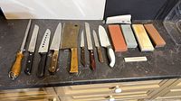 Full lineup of knives, honing steel and sharpening stones on counter
