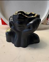 Front view of black figure-shaped trinket box showing open top and gold leaf on rim