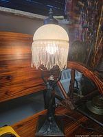 Lamp lit, showing metal figure, shade, bead fringe
