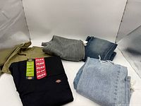 Stack of five folded pants showing black Dickies Flex, olive green, grey, dark blue and light blue jeans
