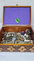 Open wooden cigar box showing loose foreign coins, keychains, rose ornament