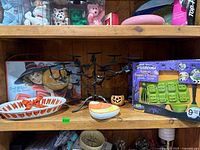 Shelf showing black metal candelabra, jack-o-lantern holder, candy-corn dish, white ribbon-candy dish, hanging witch sign and two Trudeau baking set boxes