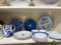 Shelf with all blue and white ceramic pieces including pitcher, divided plate, flow blue plate, dinner and side plates