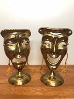 Front view of both brass comedy and tragedy masks on stands