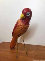 Full view of painted cement parrot sculpture standing on metal legs