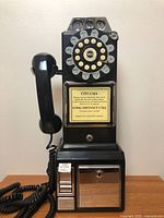 Full view of black rotary payphone replica showing handset, coin slots, coin compartment