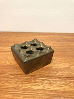 angled view of brass ashtray showing geometric recesses and patina