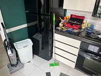Vacuum, trash can, Swiffer mop beside fridge