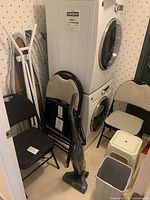 All items grouped beside washer/dryer: folding chairs, Hoover vacuum, step stool, waste bin visible