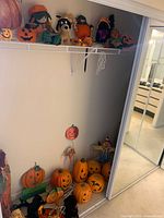 Closet showing top shelf and floor with multiple Halloween decorations including plush figures, plastic pumpkins, wooden scarecrow and yard stakes