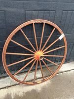 Full view of wooden wagon wheel leaning on wall showing spokes and rim