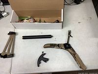 All accessories laid out including box with vanes, broadheads and wax; arm guard, black thumb release, black cylinder, camo wrist release
