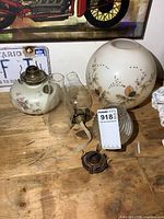 Group shot of milk glass oil lamp base with burner, floral globe, clear ribbed globe, two chimneys, spare burner